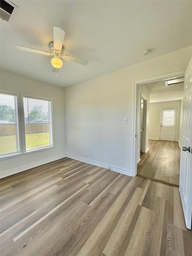 empty room featuring light wood-style floors, baseboards, a ceiling fan, and visible vents