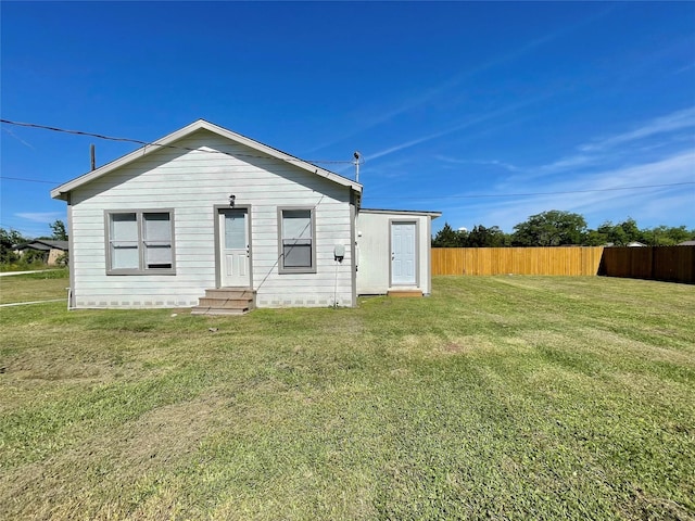 rear view of property featuring a lawn, fence, and entry steps