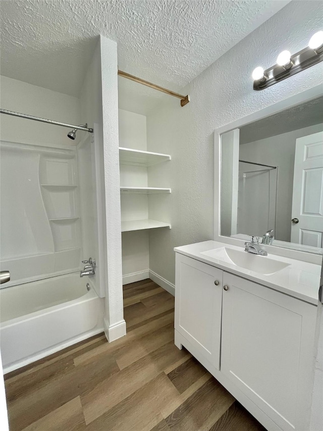 bathroom featuring a textured wall, vanity, a textured ceiling, bathing tub / shower combination, and wood finished floors