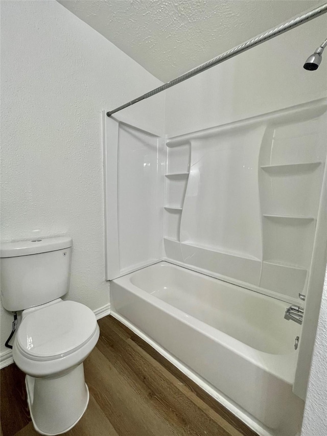 bathroom featuring toilet, a textured ceiling, baseboards, shower / bath combination, and wood finished floors