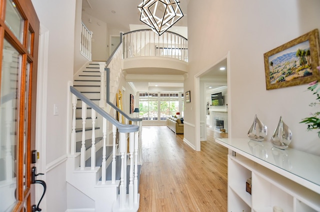 foyer with a towering ceiling, a fireplace, light wood-type flooring, stairway, and a notable chandelier