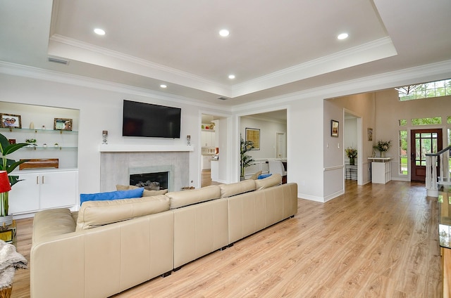 living area featuring light wood-style flooring, a raised ceiling, a glass covered fireplace, and ornamental molding