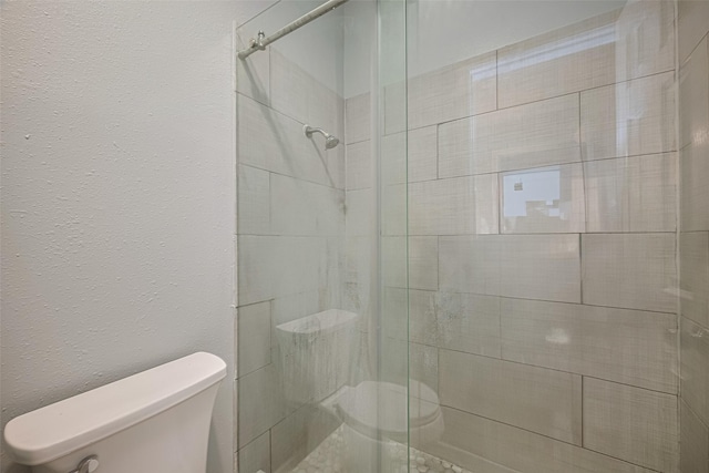 bathroom with a textured wall, toilet, and a shower stall