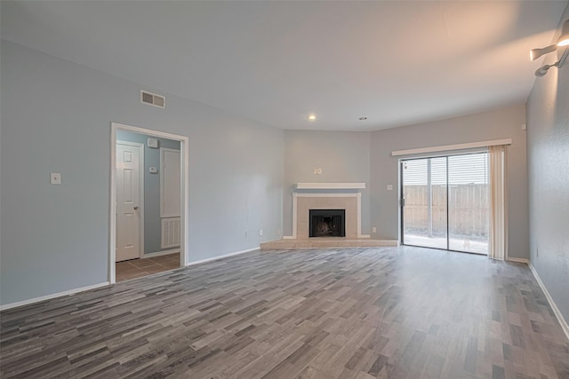 unfurnished living room with a tiled fireplace, baseboards, wood finished floors, and visible vents