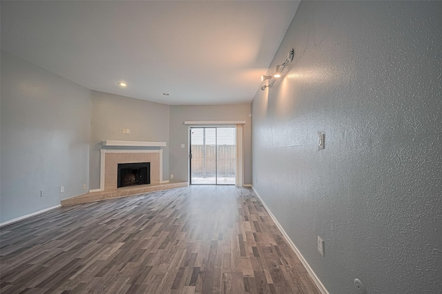 unfurnished living room featuring baseboards, a textured wall, wood finished floors, and a tile fireplace