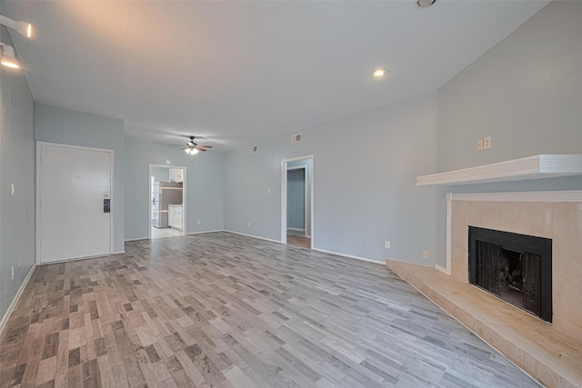 unfurnished living room with baseboards, ceiling fan, recessed lighting, a tiled fireplace, and light wood-style flooring