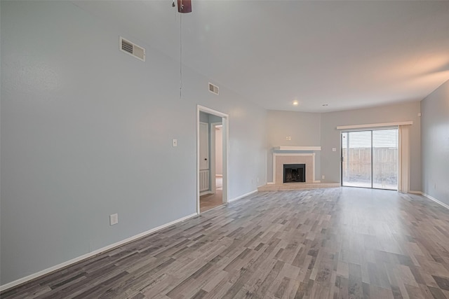 unfurnished living room with visible vents, a fireplace with raised hearth, baseboards, and wood finished floors