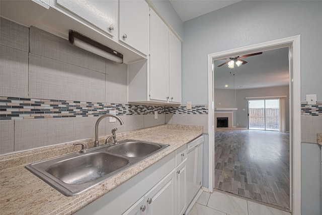 kitchen featuring ceiling fan, a fireplace, dishwasher, a sink, and white cabinets