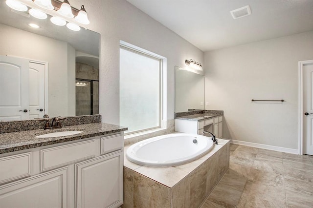 full bath with a sink, baseboards, two vanities, a garden tub, and a stall shower