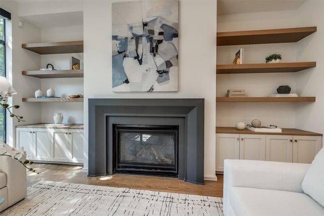living area with built in features, a glass covered fireplace, and wood finished floors