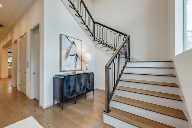 stairs featuring baseboards, visible vents, wood finished floors, and a towering ceiling