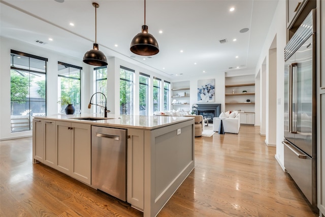 kitchen featuring a sink, a glass covered fireplace, light wood-style flooring, stainless steel appliances, and visible vents