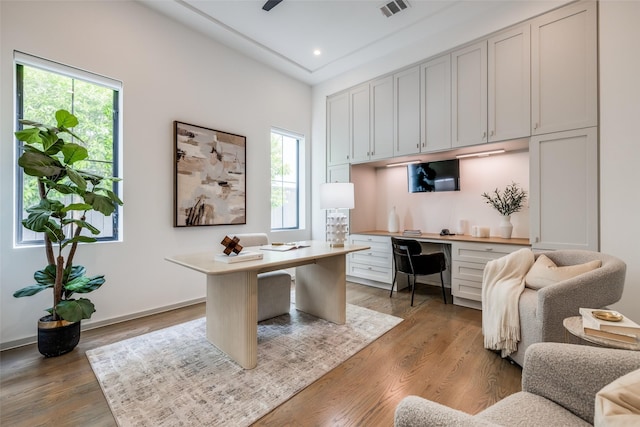 home office featuring visible vents, light wood-style floors, built in desk, and a wealth of natural light
