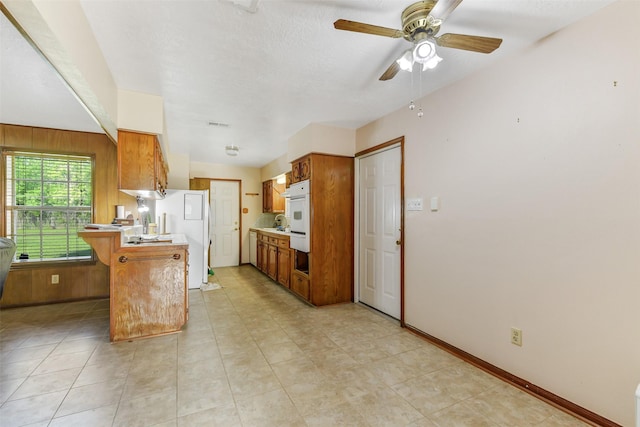 kitchen with a peninsula, oven, ceiling fan, light countertops, and brown cabinets