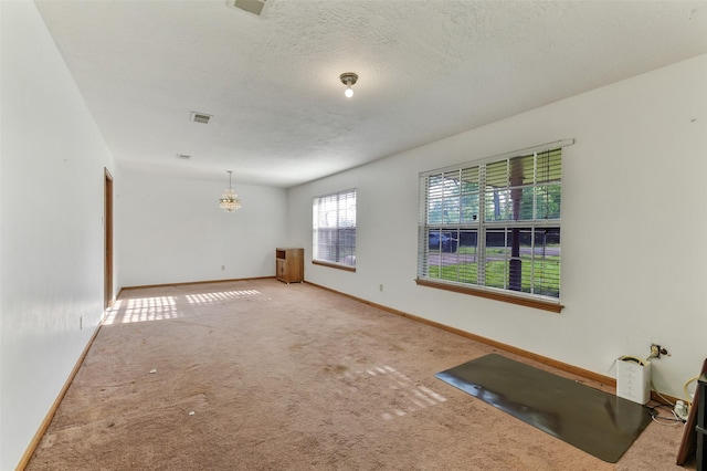 unfurnished living room with visible vents, baseboards, a textured ceiling, a chandelier, and carpet flooring