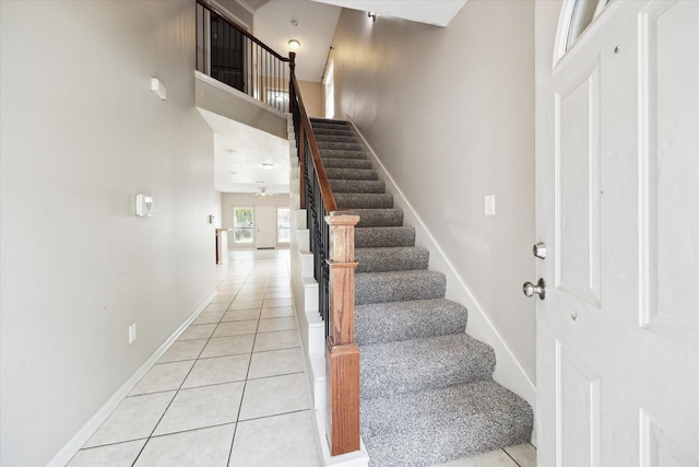 staircase featuring baseboards, tile patterned flooring, a ceiling fan, and a towering ceiling