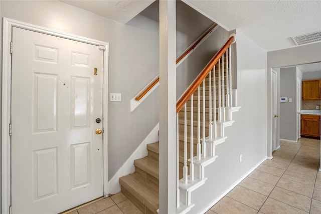 foyer with visible vents, baseboards, stairway, a textured ceiling, and light tile patterned floors