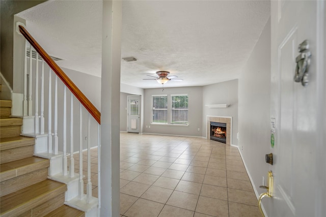unfurnished living room featuring ceiling fan, a textured ceiling, visible vents, a tile fireplace, and light tile patterned floors