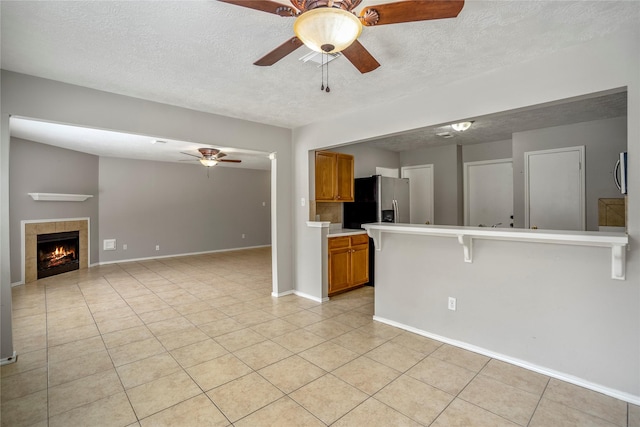 interior space featuring a ceiling fan, a textured ceiling, a tiled fireplace, and light tile patterned flooring