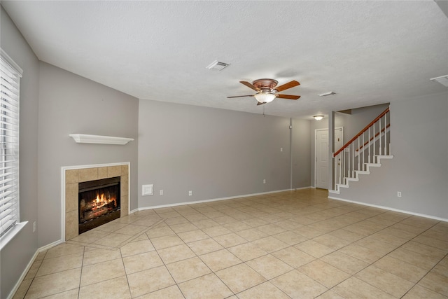 unfurnished living room with a ceiling fan, visible vents, plenty of natural light, and a tile fireplace