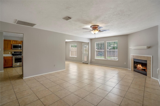 unfurnished living room featuring ceiling fan, a fireplace, a textured ceiling, light tile patterned floors, and visible vents