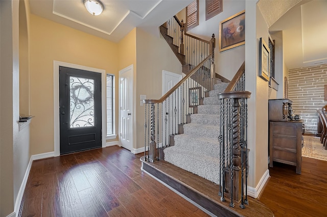 foyer featuring stairway, baseboards, arched walkways, and wood finished floors