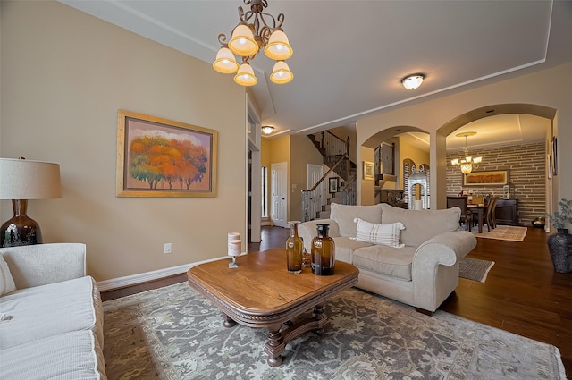 living room featuring wood finished floors, baseboards, stairway, a chandelier, and arched walkways
