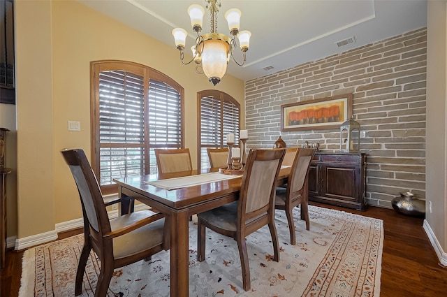 dining area featuring visible vents, wood finished floors, a chandelier, and brick wall