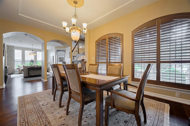 dining space with arched walkways, dark wood finished floors, baseboards, a notable chandelier, and a tray ceiling
