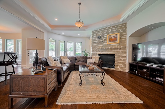 living area featuring a tray ceiling, a brick fireplace, dark wood-type flooring, and a wealth of natural light