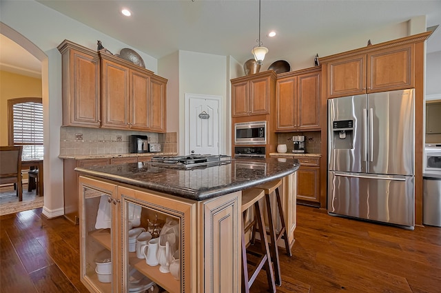 kitchen with decorative backsplash, dark wood-type flooring, brown cabinets, arched walkways, and appliances with stainless steel finishes