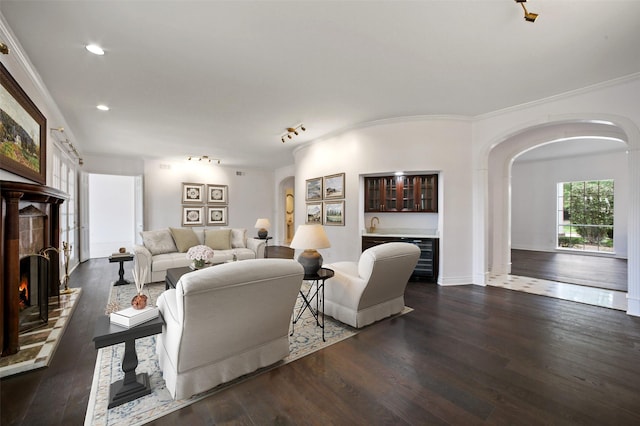 803 Mahogany Run Dr, Katy, TX 77494 - living room with arched walkways, wet bar, dark wood-type flooring, a warm lit fireplace, and crown molding