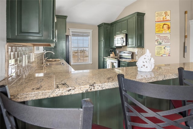 kitchen with lofted ceiling, green cabinetry, a sink, appliances with stainless steel finishes, and backsplash
