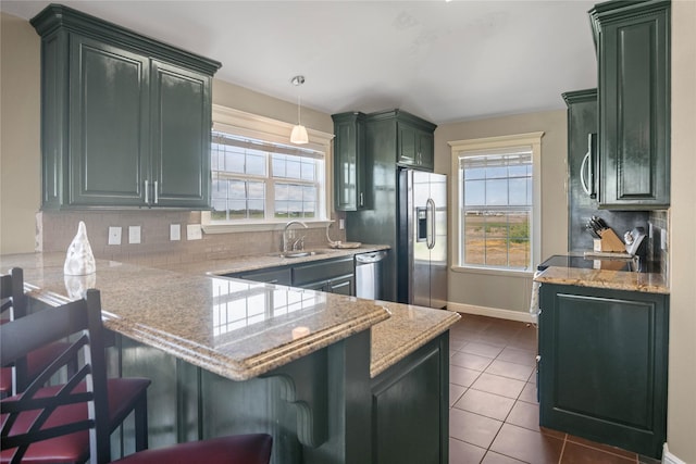 kitchen with appliances with stainless steel finishes, a sink, a peninsula, baseboards, and decorative backsplash