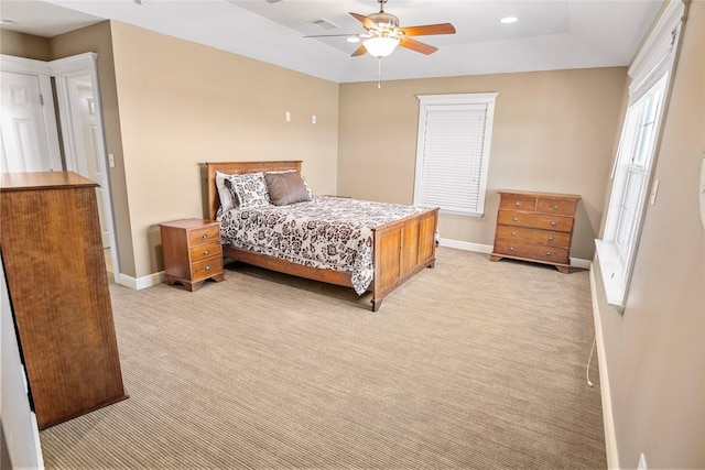 bedroom featuring visible vents, light carpet, baseboards, a tray ceiling, and a ceiling fan