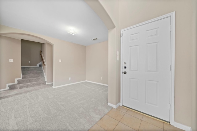 entrance foyer with light carpet, arched walkways, stairs, baseboards, and visible vents