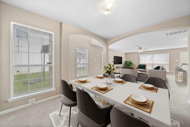 carpeted dining room with arched walkways, baseboards, visible vents, and ceiling fan