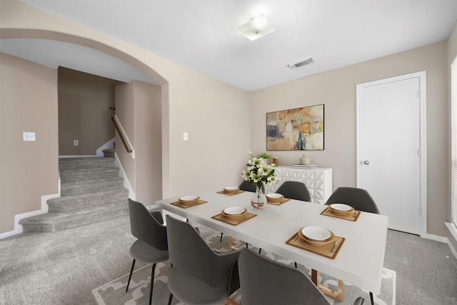 carpeted dining area with visible vents, arched walkways, stairs, and baseboards