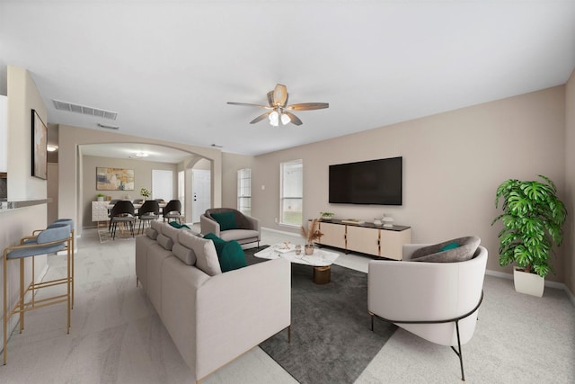 living room featuring carpet floors, arched walkways, a ceiling fan, baseboards, and visible vents