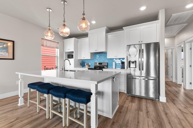 kitchen featuring visible vents, a kitchen island with sink, tasteful backsplash, a sink, and appliances with stainless steel finishes