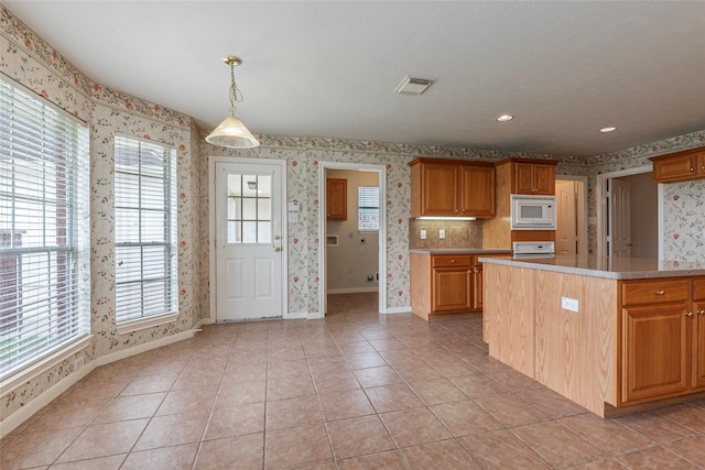 kitchen featuring light countertops, wallpapered walls, baseboards, white microwave, and visible vents