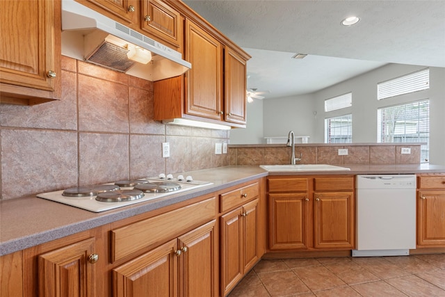 kitchen featuring decorative backsplash, white appliances, light countertops, under cabinet range hood, and a sink