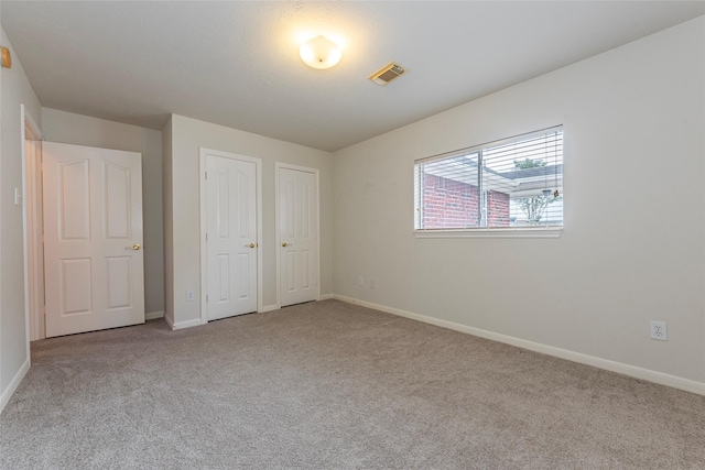 unfurnished bedroom featuring carpet floors, baseboards, and multiple closets