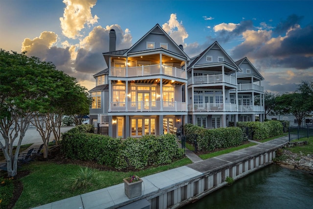 back of property at dusk featuring a standing seam roof, french doors, metal roof, a chimney, and a balcony
