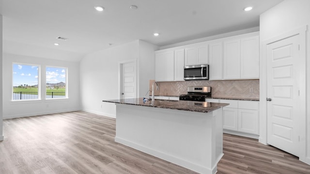 kitchen featuring decorative backsplash, a kitchen island with sink, visible vents, appliances with stainless steel finishes, and dark stone counters