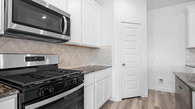kitchen with gas range oven, white cabinetry, stainless steel microwave, dark stone counters, and light wood-style flooring