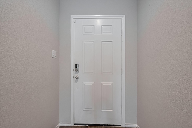 doorway to outside with baseboards, a textured wall, and wood finished floors
