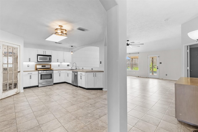kitchen with appliances with stainless steel finishes, white cabinetry, open floor plan, decorative backsplash, and visible vents