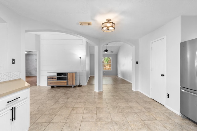 unfurnished living room featuring visible vents, baseboards, arched walkways, a ceiling fan, and light tile patterned floors