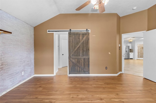 spare room featuring wood finished floors, ceiling fan, lofted ceiling, and brick wall